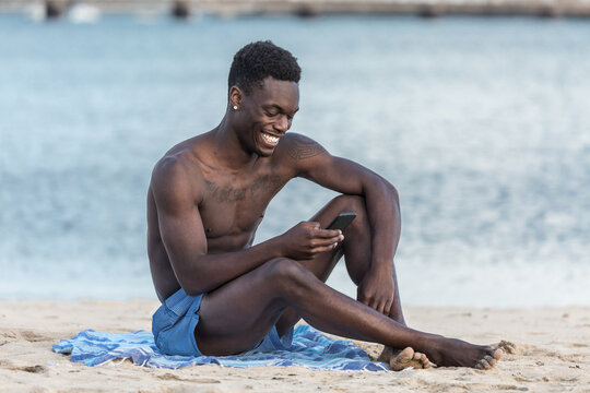 Cheerful African American man using smartphone on beach
