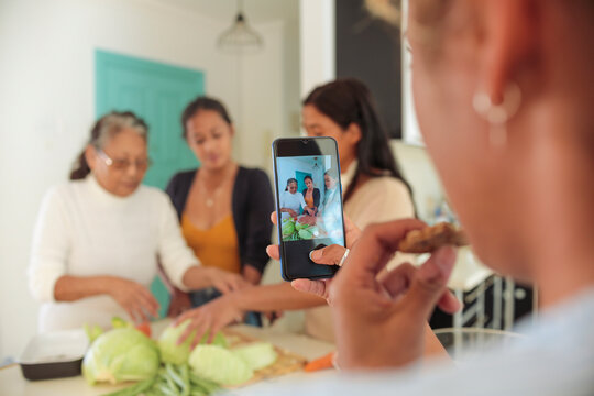 Filipino family cooking together at home - Girl taking a video of her grandmother and mother showing a recipe to her sister