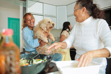 Filipino family cooking together at home - Young woman hugging her dog while her grandmother is cooking in the kitchen - Family of three women spending quality time together - 422829781
