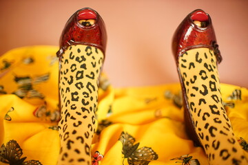 Female legs in leopard print tights and red patent leather shoes on a yellow pink bed