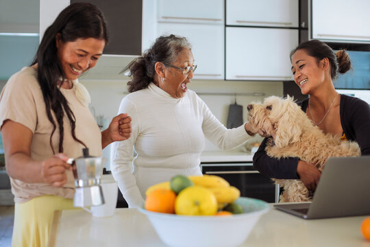 Filipino family of three women having breakfast at home together before start to work - Grandmother and granddaughter playing with the dog