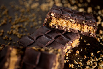 Broken assorted chocolate bar with carrot cake filling with cashew nuts around on a wooden table. Gourmet. Close up.