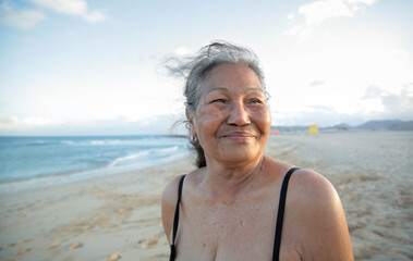 Beautiful senior woman standing at the beach, wearing a black bikini - Filipino mature woman smiling and enjoying her time on vacation - 422830998