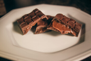 Broken assorted chocolate bar with caramel filling on a white plate. Gluten free. Close up. Gourmet. 