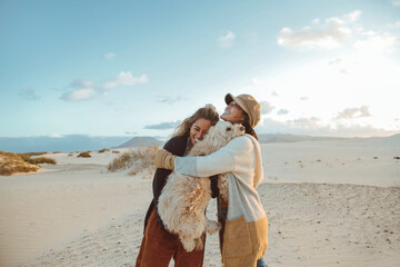 Two beautiful filipino women laughing and hugging each other and their dog - Friends having a great time together walking in a desert - 422831178