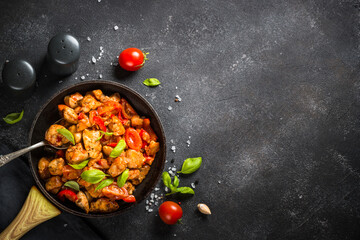 Chicken meat with vegetables in tomato sauce on black.