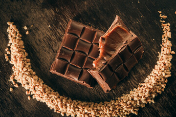 Top view of a broken assorted chocolate bar with caramel filling. Peanuts around in a moon shape. Gluten free. Gourmet. 