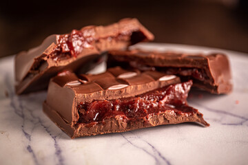Broken chocolate bar with strawberry jam filling on a marble board. Gourmet. Close up.