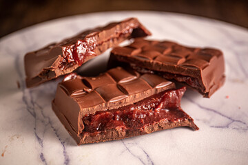 Broken chocolate bar with strawberry jam filling on a marble board. Gourmet. Close up.
