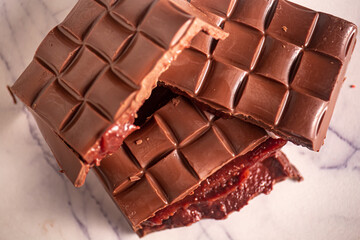 Broken chocolate bar with strawberry jam filling on a marble board. Gourmet. Close up. Top view.