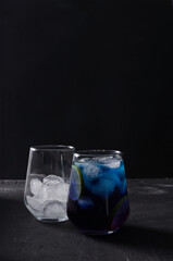 Blue cold drink with pieces of ice in a transparent glass on a black background in a dark key, vertical background
