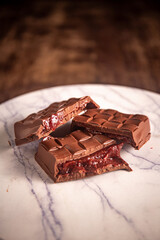 Broken chocolate bar with strawberry jam filling on a marble board. Gourmet. Close up. Space for text.