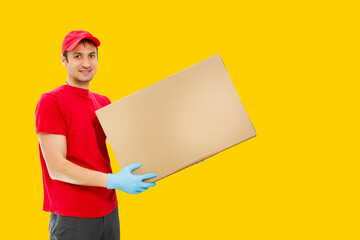 Portrait of delivery man in red uniform holding parcel box isolated over yellow background