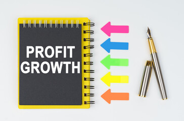 On a white background lies a pen, arrows and a notebook with the inscription - PROFIT GROWTH