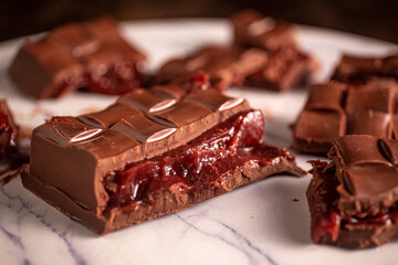 Broken chocolate bar with strawberry jam filling scattered on a marble board. Gourmet.