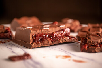 Broken chocolate bar with strawberry jam filling scattered on a marble board. Gourmet.