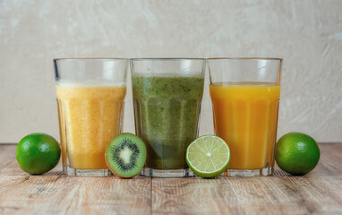 Three tall glass with kiwi and spinach smoothies in a row surrounded by fruits