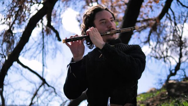 Man in Medieval outfit playing flute, rocking back and forth. 4k, 60fps, slow motion, tracking shot