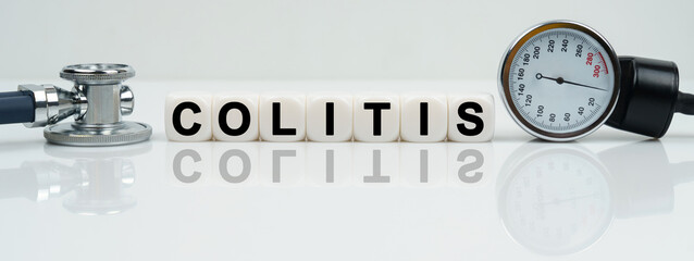 On a reflective white surface lies a stethoscope and cubes with the inscription - COLITIS