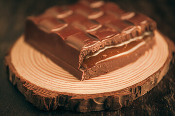 Tasty broken chocolate bar with passion fruit filling on a tree trunk on a wooden table. Close up. Selective focus. 