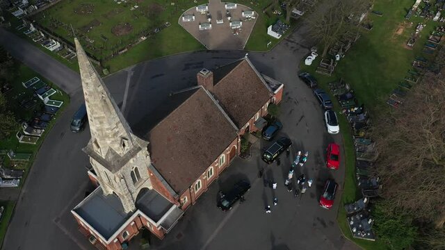 TILT DOWN SHOT OF FAMILIES AND FUNERAL VAN INFRON OF A CHURCH IN THE CEMETERY