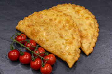 Chebureks on a black background. Served with cherry tomatoes. Caucasian cuisine.