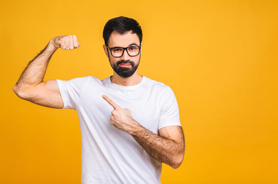 Portrait of a happy young bearded man dressed in t-shirt showing biceps isolated over yellow background.