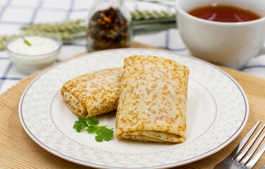 Pancakes rolled up in an envelope on a plate. Served with sour cream and a cup of tea on a napkin.