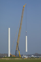 A crawler crane is hoisting the tower of a new wind turbine