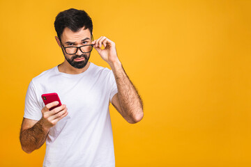 Always in touch. Happy young amazed shocked bearded man in glasses typing sms on yellow background.