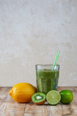 Tall glass with kiwi and spinach smoothie surrounded by fruits on a wooden table