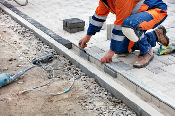 The bricklayer uses a black marker and an aluminum level to measure out a portion of the paving slabs for alignment on the sidewalk.