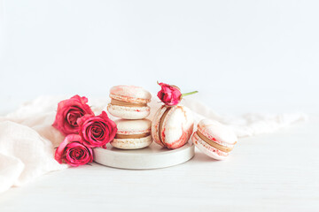 Tasty french macaroons with pink roses on a white wooden background.
