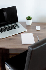 Office at home. Laptop, notebook, pen are on the table near the white wall.
