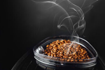 fresh roasted coffee beans with smoke in coffeemaker bean container, close-up view