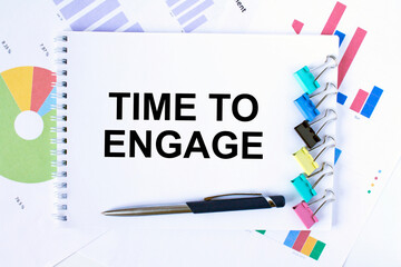 Notepad with text Time To Engage, paper clips, blue pen on financial diagrams