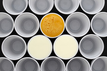White plastic disposable cups filled with milk and orange juice, view from above