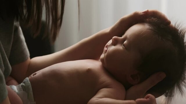 Authentic young mother holds new born baby in her arms, strokes his hair while he sleeps, lulls him to sleep with tenderness and care for the child. Maternity and motherhood concept.