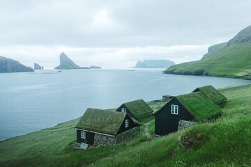 Picturesque view of tradicional faroese grass-covered houses in the village Bour. Drangarnir and Tindholmur sea stacks on background. Vagar island, Faroe Islands, Denmark. Landscape photography