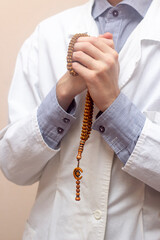 A young man in a white robe raised his hands up and prayed with a Muslim rosary. Beige background. Doctor praying. A Muslim makes dua.