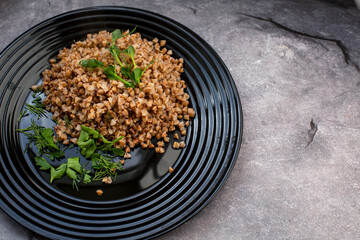 boiled buckwheat porridge with herbs and sprouts of peas on a black plate. vegetarian dish