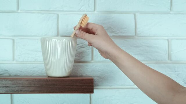 Health material toothbrush. A woman use a wooden organic teethbrush and puts it into a glass in the bathroom.