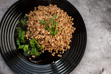 boiled buckwheat porridge with herbs and sprouts of peas on a black plate. vegetarian dish