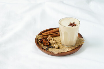 masala chai or Indian spices tea in transparent glass placed on a circle brown wooden tray beside dried spices
