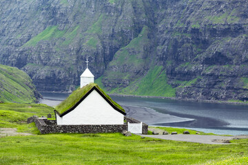 Obraz premium Summer view of traditional turf-top church Saksunar Kirkja in Saksun village. Beauty landscape with Pollurin Laguna and high mountains. Streymoy island, Faroe Islands, Denmark