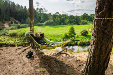 Fototapeta na wymiar Man resting in a hammock on the high bank of the river alone