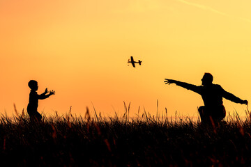Silhouettes of a father and a little son playing with a toy plane at sunset background.