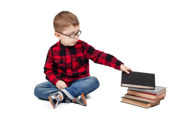 A little boy with glasses picks up a book from a stack of books, isolated on white background.