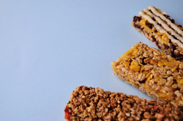 Three bars of granola lie fan in the bottom right corner on a blue background close-up with a copy space. High quality photo