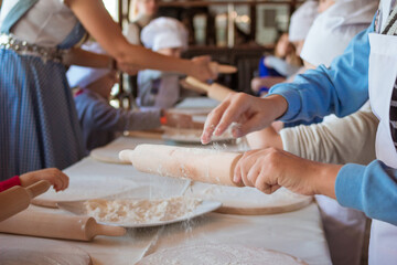 Obraz na płótnie Canvas Cooking class, culinary. Kids hands in uniform preparing dough for pizza or bread. Hand puts dough yeast on a wooden cutting board sprinkled with flour. Children preparing food, meal in the kitchen